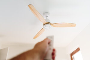 A modern ceiling fan and a hand with its remote control in the foreground.