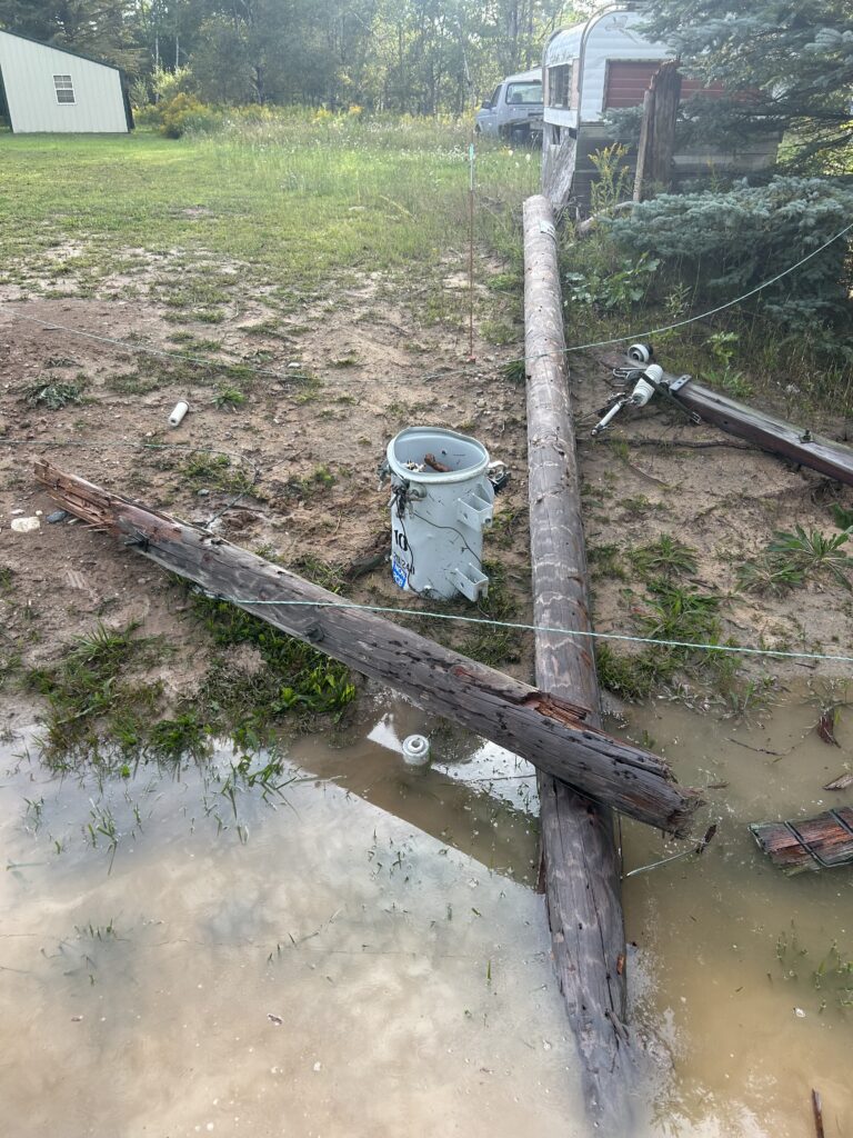 Broken electric pole with lines down around water due to storm damage.