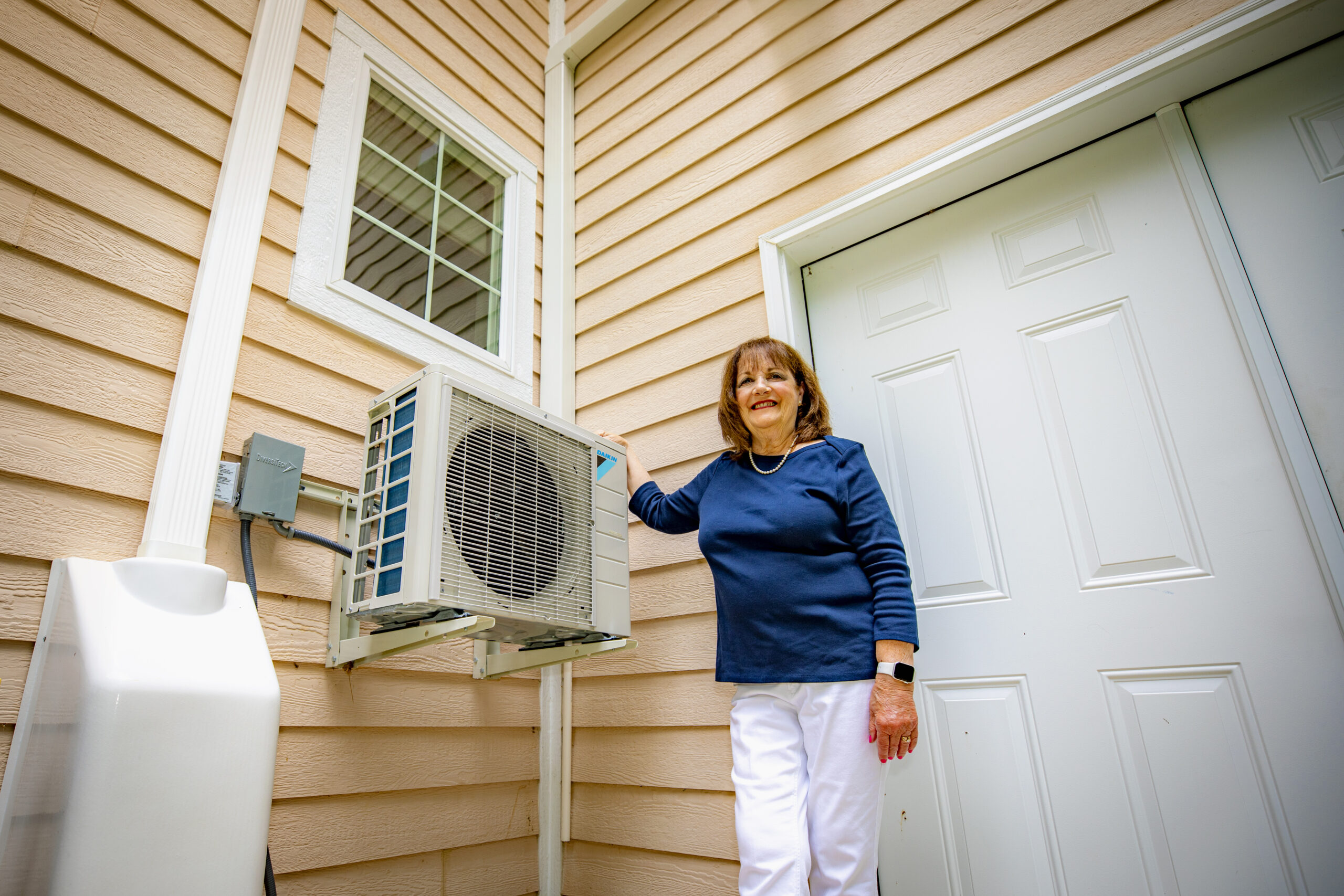 Woman standing next to her outdoor compressor for mini-split heating and cooling unit.