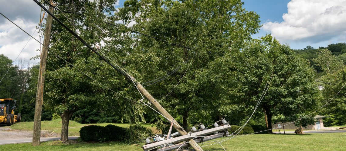 Broken snapped wooden power line post with electrical components on the ground after a storm