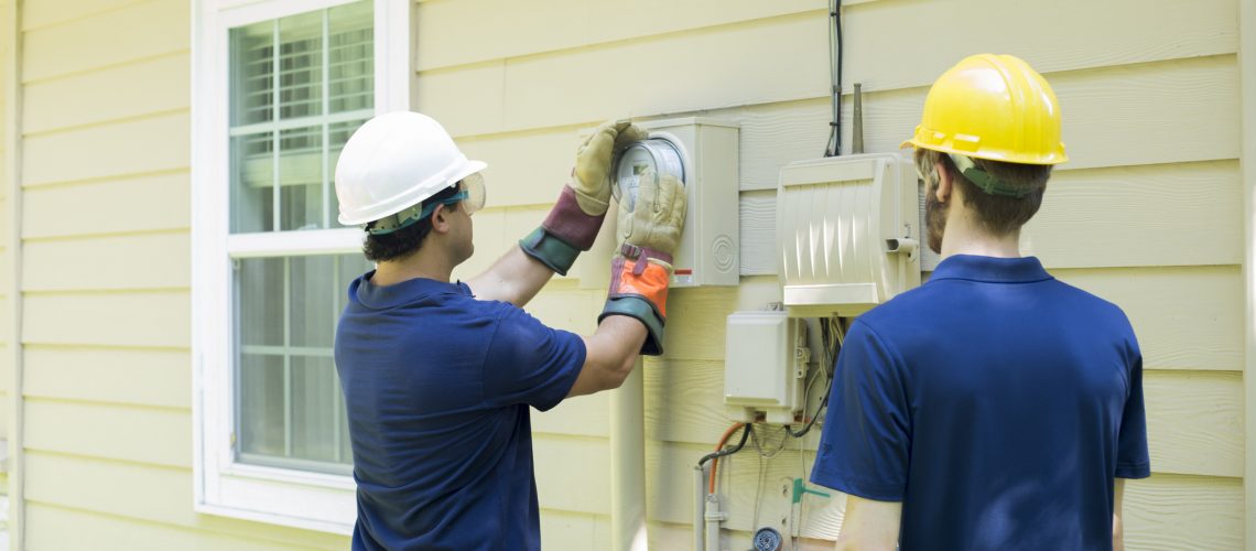 Electrical repair man working on outside meter of home.