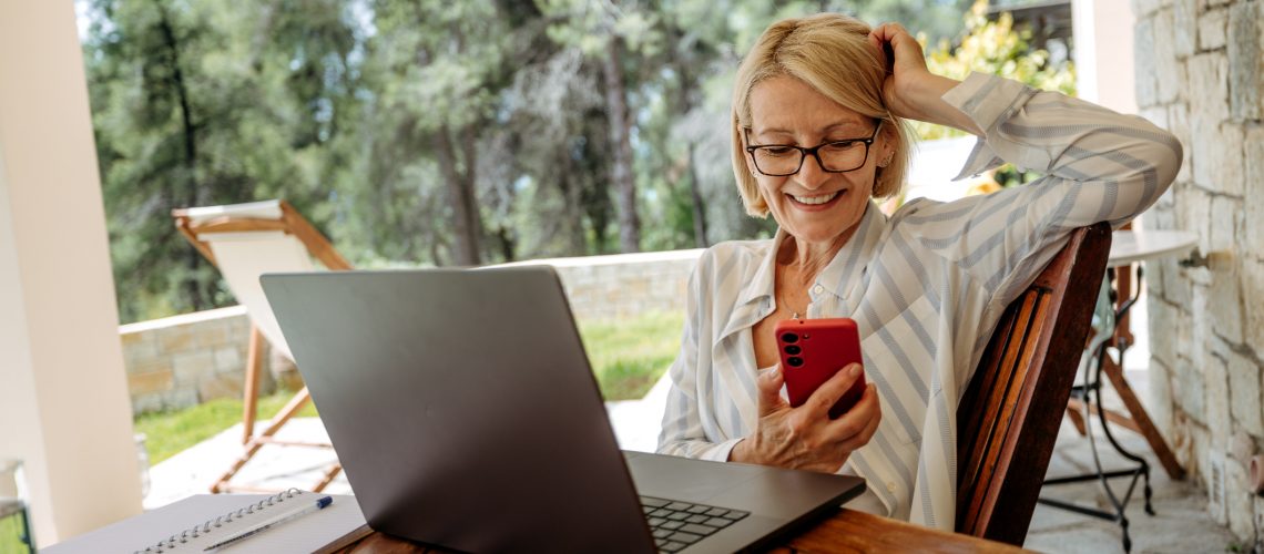 Smiling mature businesswoman using smart phone while working from back yard of her home