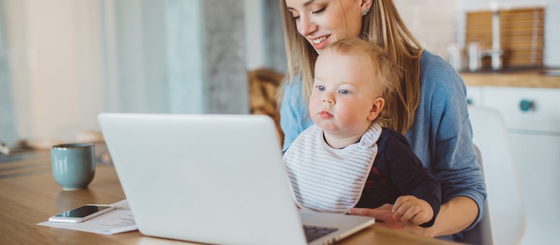 Mother with baby paying bills online. They are in the kitchen, ejoying in the mornong.