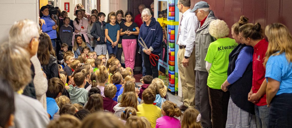 Kiwanis Club of Charlevoix Board President Gail Gennett holds an oversized pair of scissors as she speaks during a ribbon-cutting ceremony in October for a new book vending machine at Charlevoix Elementary School.